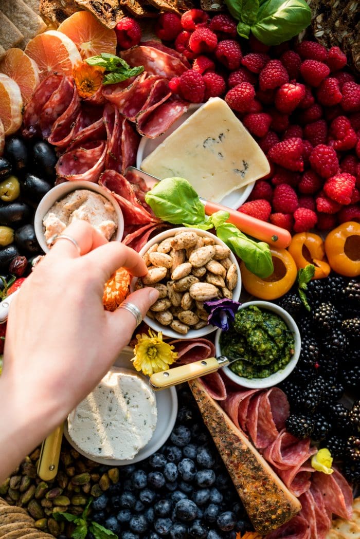 hand reaching into almond bowl on a beautiful colorful charcuterie