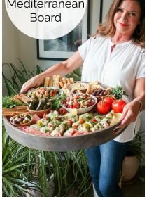 woman holding a dark gray round Epic Summer Mediterranean Board filled with charcuterie snacks