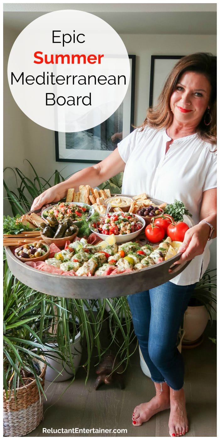 woman holding a dark gray round Epic Summer Mediterranean Board filled with charcuterie snacks