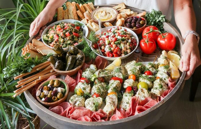 a person holding a big board filled with Mediterranean food