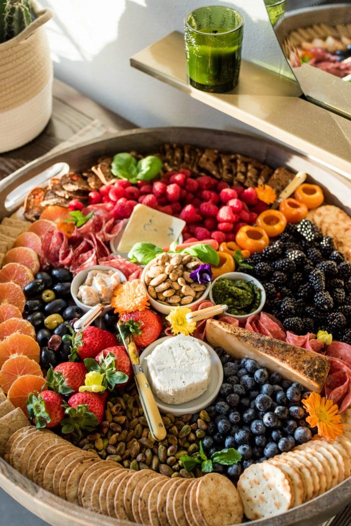looking down on a big round wood board filled with "rainbow" colored foods and charcuterie