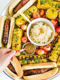 dipping a spoon into mustard on a Summer Brats and Sauerkraut Tray