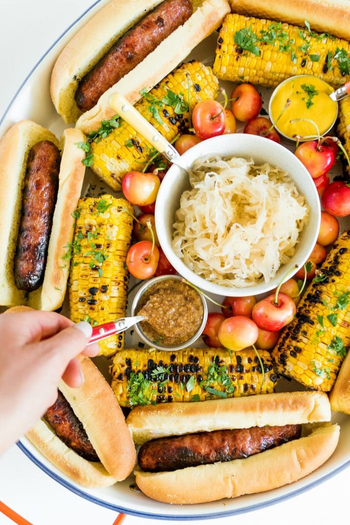 dipping a spoon into mustard on a Summer Brats and Sauerkraut Tray