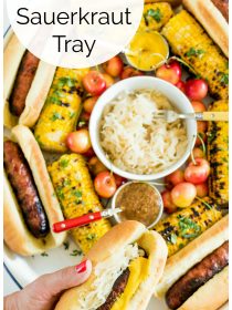 a tray filled with grilled brats, sauerkraut, grilled corn, and cherries