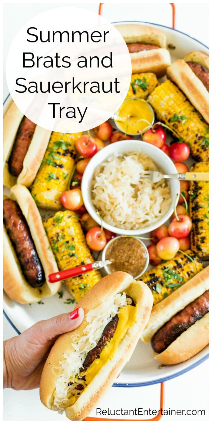 a tray filled with grilled brats, sauerkraut, grilled corn, and cherries
