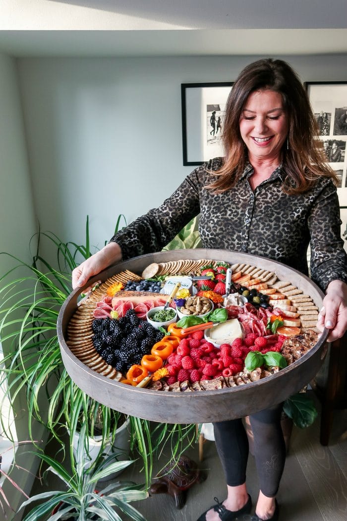 woman holding a big board of charcuterie with colorful foods