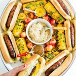 holding a Summer Bratwurst with Sauerkraut in front of a Summer Brats and Sauerkraut Tray