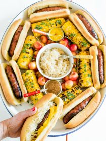 holding a Summer Bratwurst with Sauerkraut in front of a Summer Brats and Sauerkraut Tray