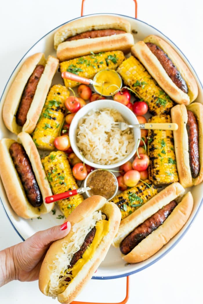 holding a Summer Bratwurst with Sauerkraut in front of a Summer Brats and Sauerkraut Tray