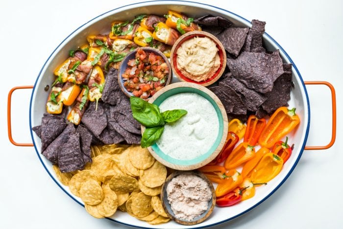 oval platter of chips with hummus, ranch dressing, salsa, and peppers