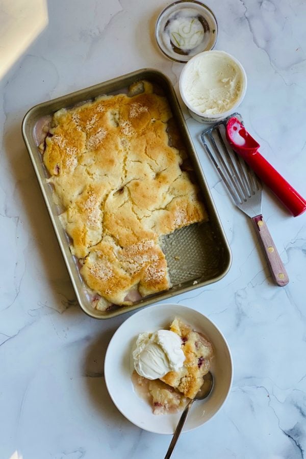 9x13 pan of peach cobbler with a serving, and vanilla ice cream