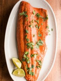 one large salmon filet on a white plate, cooked with lime and garlic, garnished with lime and cilantro