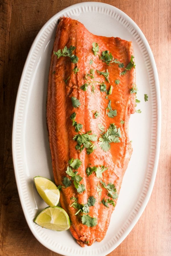one large salmon filet on a white plate, cooked with lime and garlic, garnished with lime and cilantro