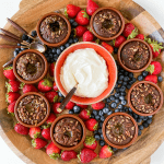 a round wood dessert board with lava cakes, fruit, and whipped cream