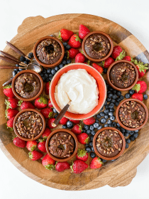 a round wood dessert board with lava cakes, fruit, and whipped cream