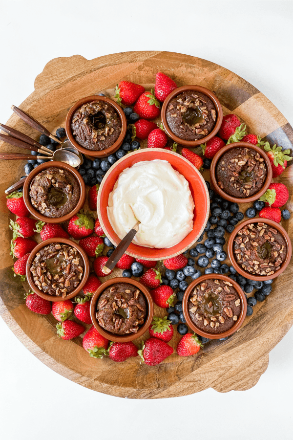 a round wood dessert board with lava cakes, fruit, and whipped cream