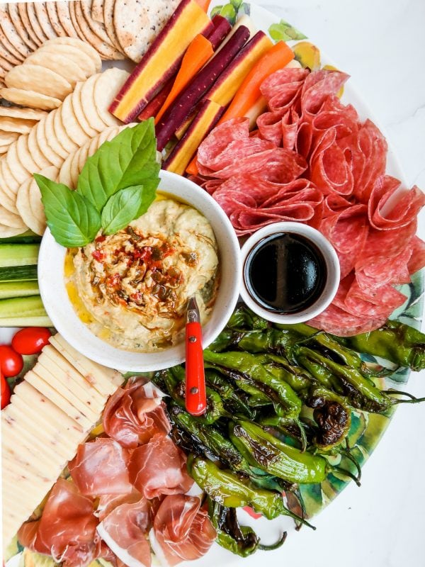 a bowl of hummus garnished with basil on a cheese board