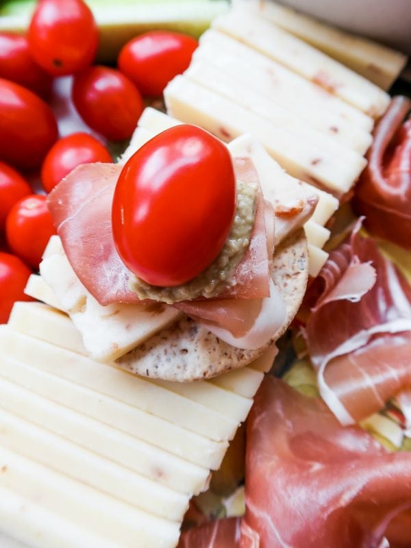 a cracker bite with cheese, meat, hummus, and tomato