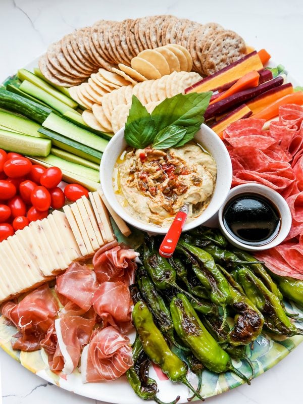 hummus on a cheese board with peppers, meat, cheese, veggies