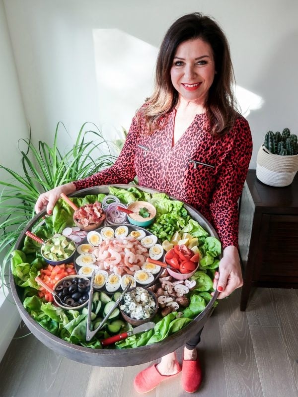 woman holding a big round wood tray filled with shrimp cobb salad ingredients for a build your own salad