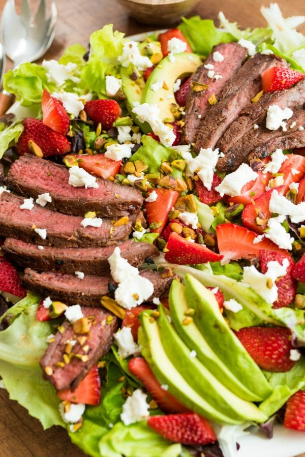 beautiful sllices of steak and avocado on bed of greens with strawberries