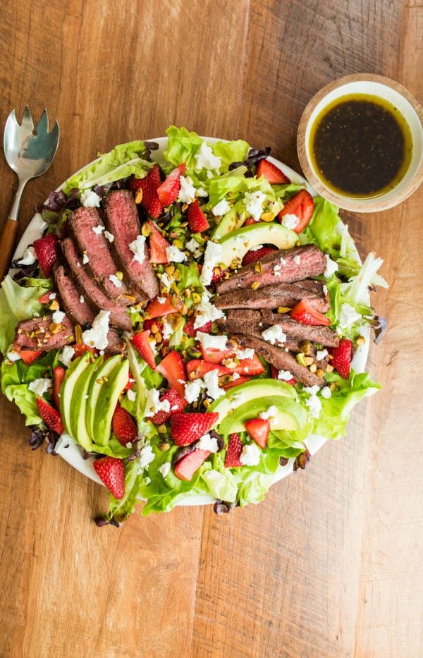 sliced steak on a bed of greens with strawberries, avocados and balsamic dressing