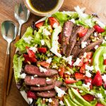 grilled steak salad with strawberries and avocados and small round bowl of dressing