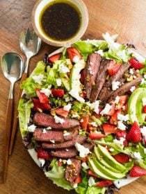 grilled steak salad with strawberries and avocados and small round bowl of dressing