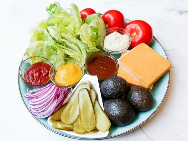 a close up of iceberg lettuce on a Basic Burger Condiment Platter, with tomatoes, avocados, cheese, red onion, etc.