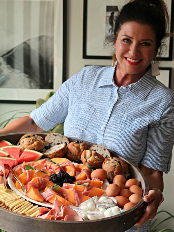 close up woman holding a Ham Cheese Brunch Board with eggs, muffins, melon, etc.