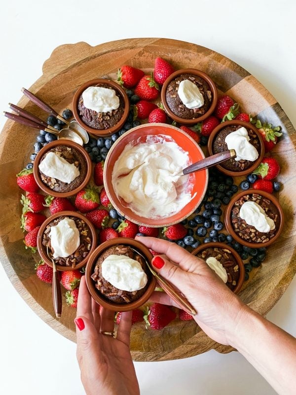 a round wood board with 8 hot lava cakes, whipped cream, berries