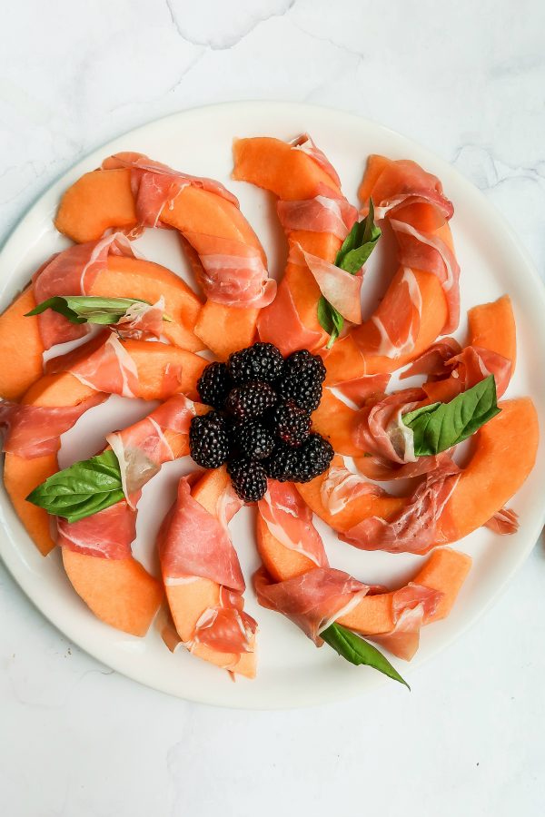 beautiful plate of Prosciutto-Wrapped Melon slices with fresh basil