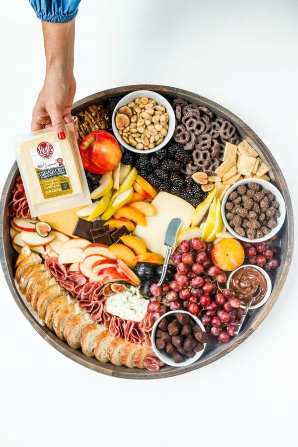 a round cheese board, holding a package of Grand Cru cheese