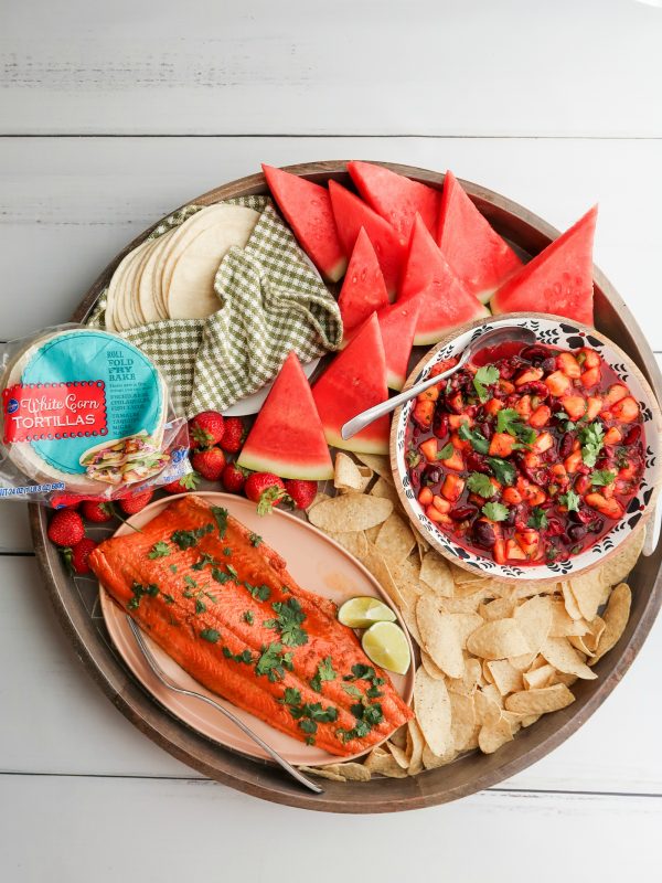 salmon, taco shells, chips on a round dinner board