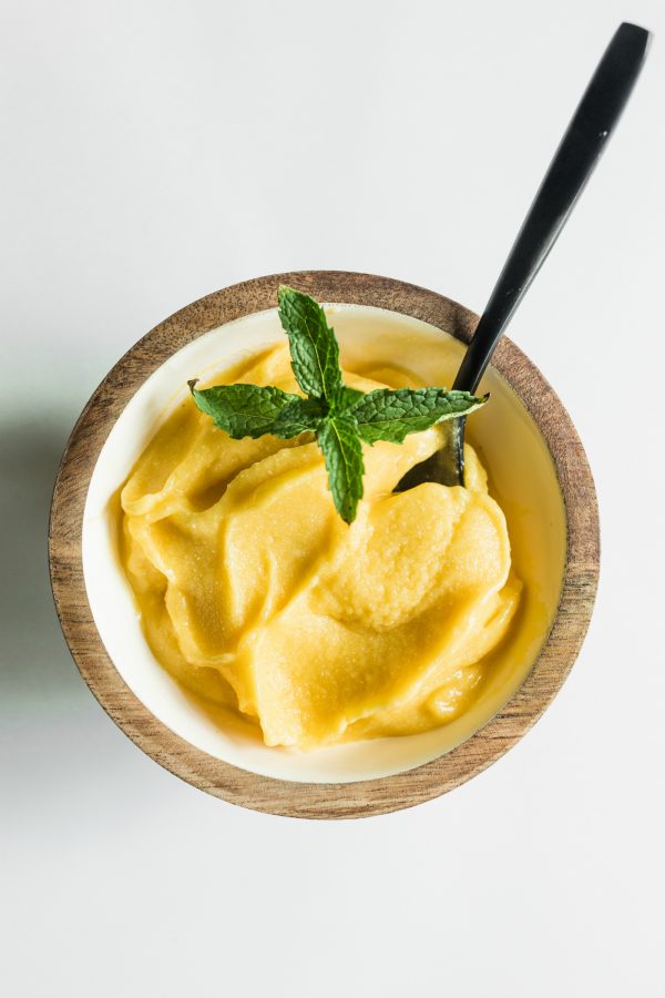 a small wood bowl with mango coconut sorbet with a spoon in it
