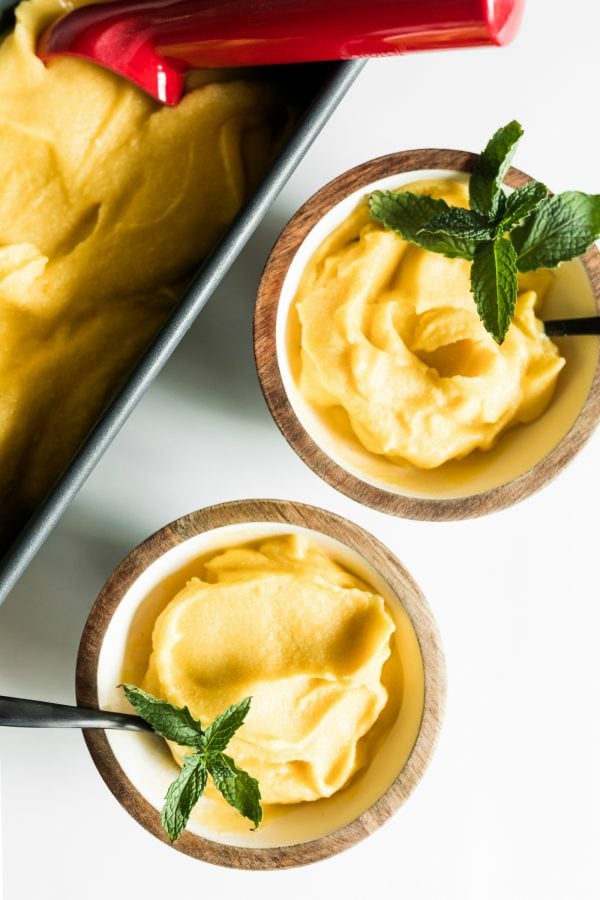 loaf pan of mango coconut sorbet with 2 bowls dish up, with spoons