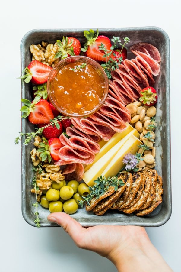easy to transport, a small baking pan of charcuterie with jam, nuts, and garnished with fruit