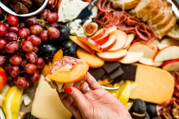 holdling a cracker with salami, Grand Cru cheese, and a nectarine