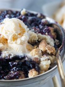 a round bowl of blueberry crunch with a scoop of vanilla ice cream