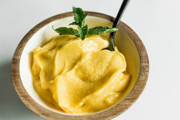 a small bowl of mango coconut sorbet with a fresh mint leaf and spoon