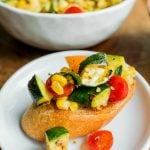 a piece of crostini toast with grilled corn, tomato, zucchini chopped in small pieces on top