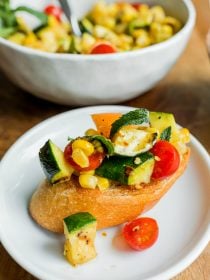 a piece of crostini toast with grilled corn, tomato, zucchini chopped in small pieces on top