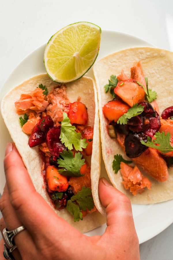 holding 2 salmon tacos with cherry peach salsa