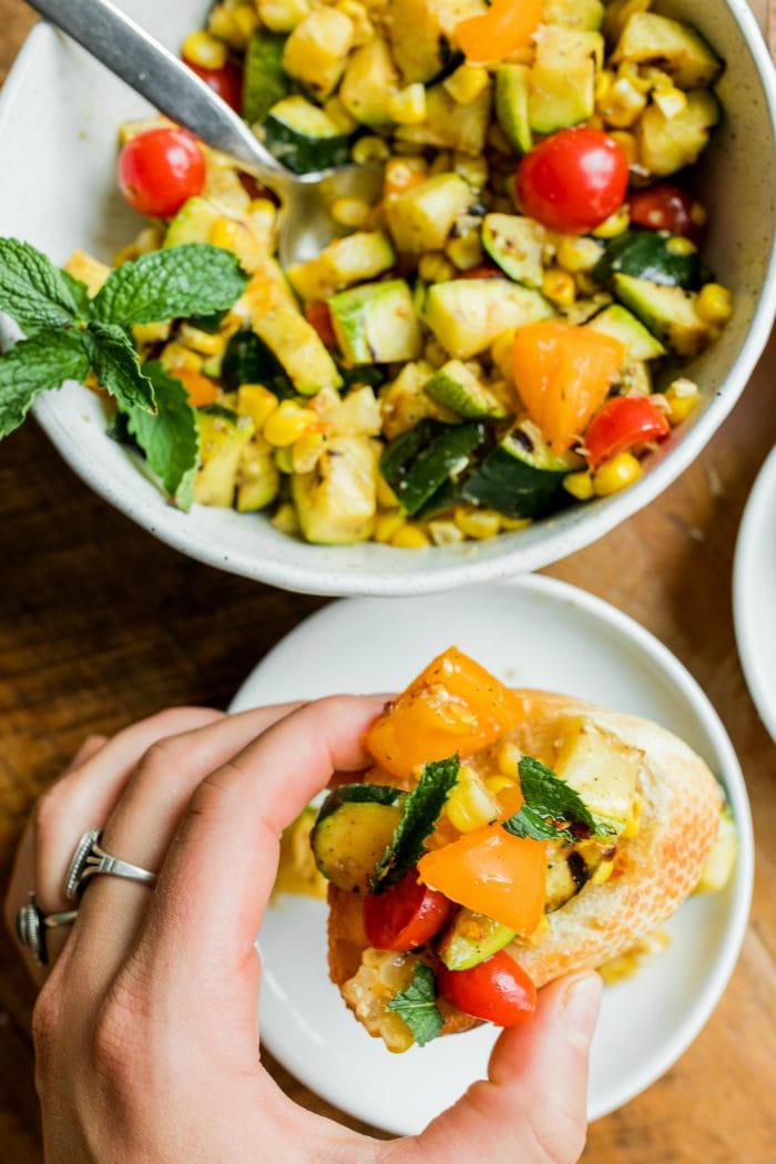holding upclose a Grilled Zucchini Corn Crostini