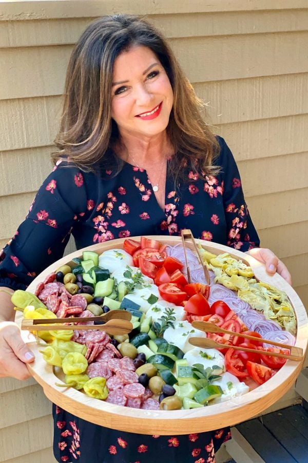 woman holding a round wood tray with deconstructed burrata choopped salad