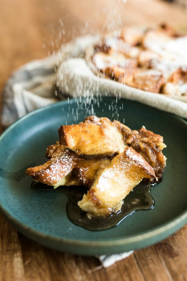 shaking powdered sugar on a serving of Banana Bread Brioche French Toast