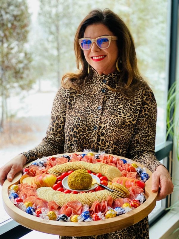 lady holding a round charcuterie board with a cheese ball incenter