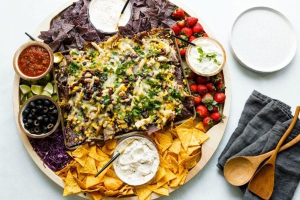 nacho board with chips, dips, and strawberries on wood board
