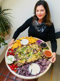 woman holding a big round board with nachos and dips