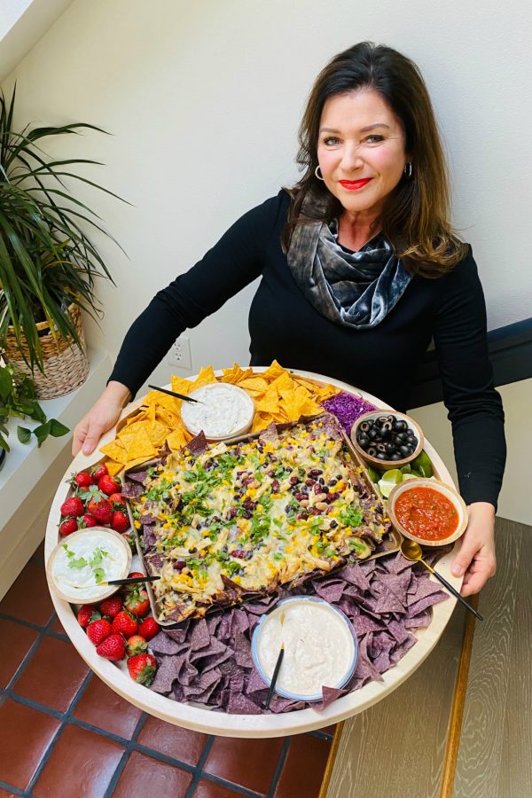 woman holding a big round board with nachos and dips